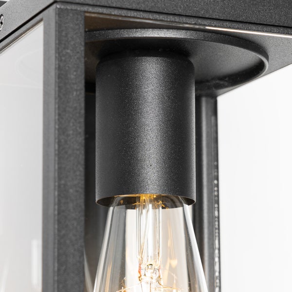 Detailaufnahme einer schwarzen Außenwandleuchte aus Metall mit Glaseinsätzen und einer klaren Edison-Glühbirne.