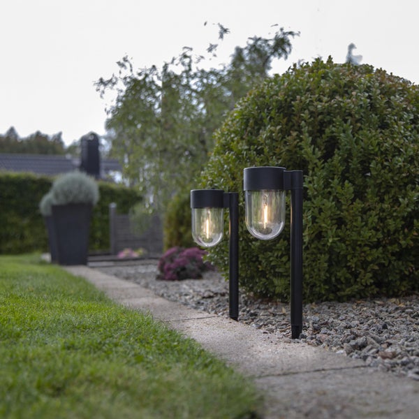 Beleuchteter Garten mit zwei Gartenleuchten entlang eines Weges.