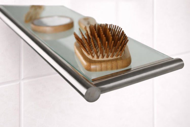Glasablage für das Badezimmer mit Edelstahlrahmen, montiert an einer gefliesten Wand, mit einer Haarbürste aus Holz.
