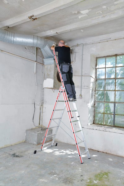 Mann steht auf einer Hymer Leiter und arbeitet an einem Lüftungskanal in einem renovierungsbedürftigen Raum.