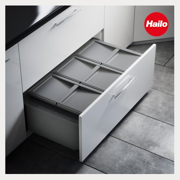 Hailo Logo. Einbau-Abfalleimer-System mit drei grauen Behältern in einem weißen Küchenauszug auf einem Fliesenboden.