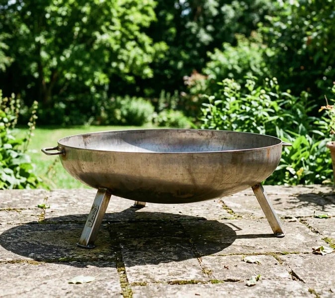Runde Feuerschale aus Metall mit drei Beinen und seitlichen Griffen für den Garten auf einer Steinterrasse.