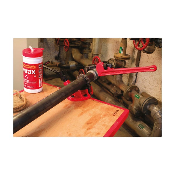 Rohrtrenngerät mit Rohrzange, Reinigungstüchern und Hanf auf einer Werkbank vor einem Rohrsystem.