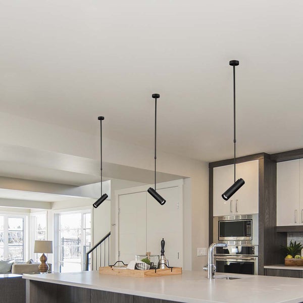 Drei schwarze, zylinderförmige Pendelleuchten über einer modernen Kücheninsel in einer hellen, offenen Küche.