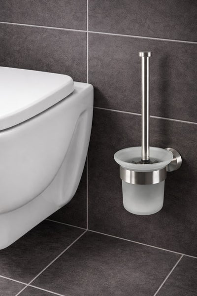 Wandmontierte WC-Garnitur aus Edelstahl und satiniertem Glas neben einer weißen Toilette an einer Wand aus dunklen Fliesen.