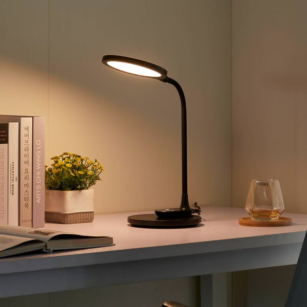 Schwarze LED Schreibtischlampe auf einem weißen Schreibtisch neben Büchern und einer Pflanze, hell beleuchteter Arbeitsplatz.