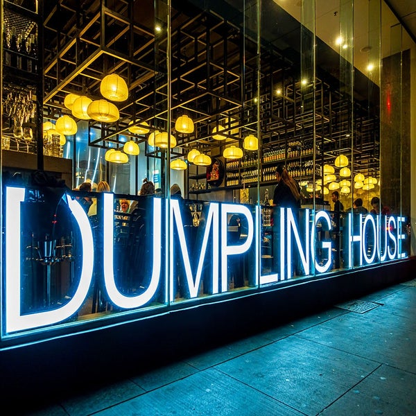 Ansicht des Eingangs zum Dumpling House mit beleuchtetem Schriftzug und Gästen im Inneren