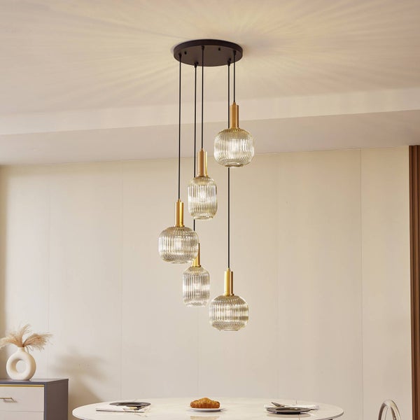 Fünfflammige Pendelleuchte mit geriffelten Glasschirmen und messingfarbenen Details, hängend über einem Esstisch in einem hellen, modernen Raum.