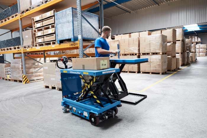 Mobiler hydraulischer Scherenhubtisch in einem Lagerhaus, beladen mit einem Karton vor hohen Regalen.