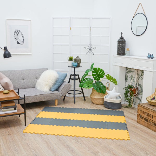 Gestreifte Puzzlematten in Grau und Gelb auf Holzboden in einem hellen, modern eingerichteten Wohnzimmer mit Sofa, Zimmerpflanzen und Dekoration.
