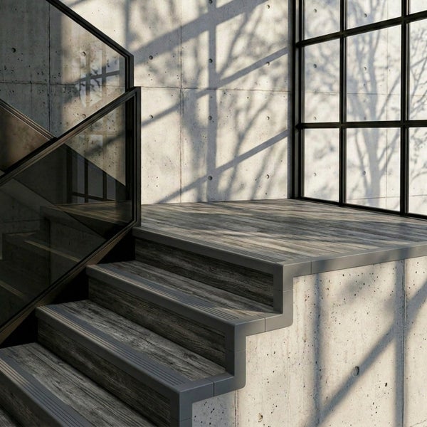 Moderne Treppe mit Stufen in Holzoptik, Sichtbetonwänden und Glasgeländer in einem hellen, industriellen Raum.