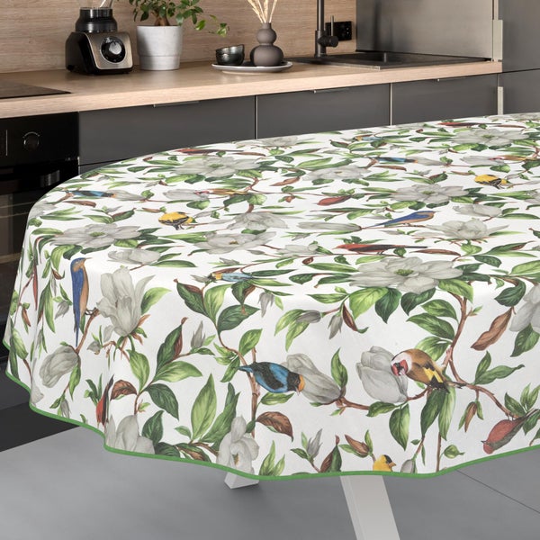 Ovale Tischdecke mit Muster aus weißen Blüten, grünen Blättern und bunten Vögeln auf Zweigen, dargestellt in einer modernen Küche.