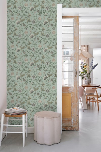 Ein Raum mit floral gemusterter Tapete, einem Hocker und einem Blick in einen hellen Essbereich.