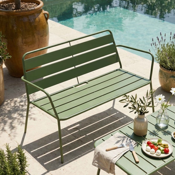 Grüne Gartenbank aus Metall mit Armlehnen auf einer sonnigen Terrasse am Pool, dekoriert mit Pflanzen und einem passenden Beistelltisch.