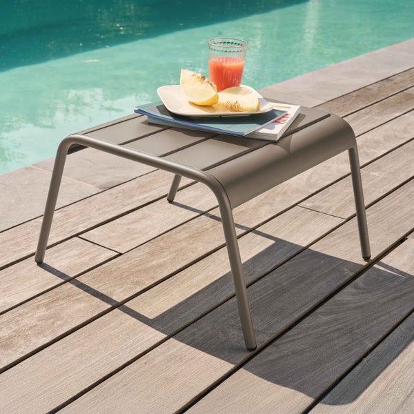 Moderner grauer Beistelltisch aus Metall auf einer Holzterrasse am Pool mit Zeitschriften und Melone.