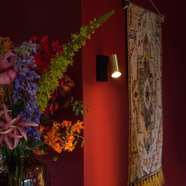 Wandleuchte neben Blumenvase und Wandteppich