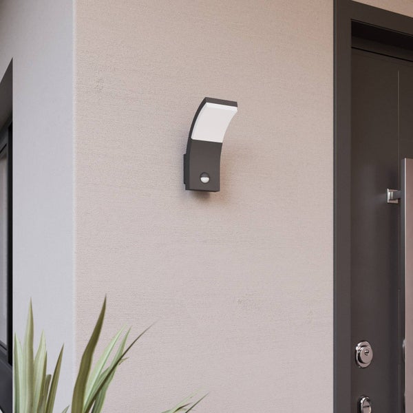 Moderne Außenwandleuchte mit Bewegungsmelder an einer Hausfassade neben einer Eingangstür.