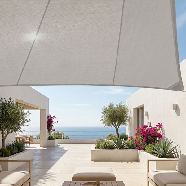 Großes Sonnensegel über einer hellen Terrasse mit Loungemöbeln, mediterranen Pflanzen und weitem Meerblick.