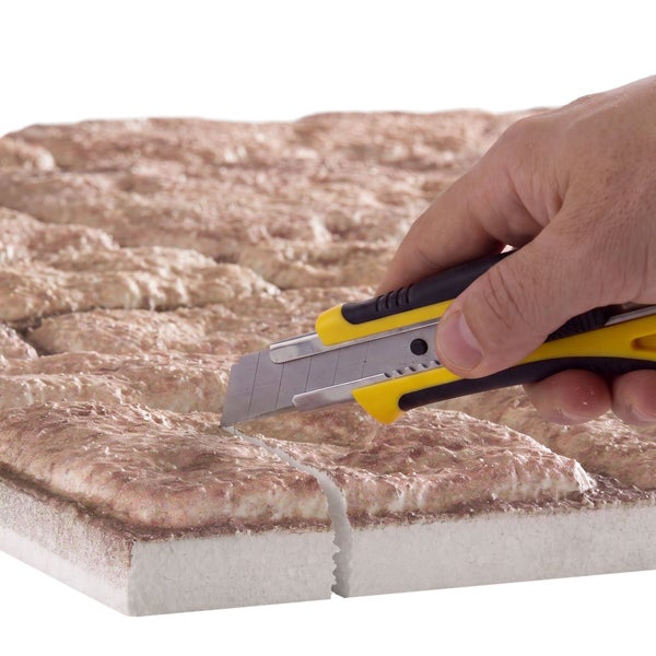 Eine Hand schneidet eine strukturierte Dämmplatte mit einem Cuttermesser zu.