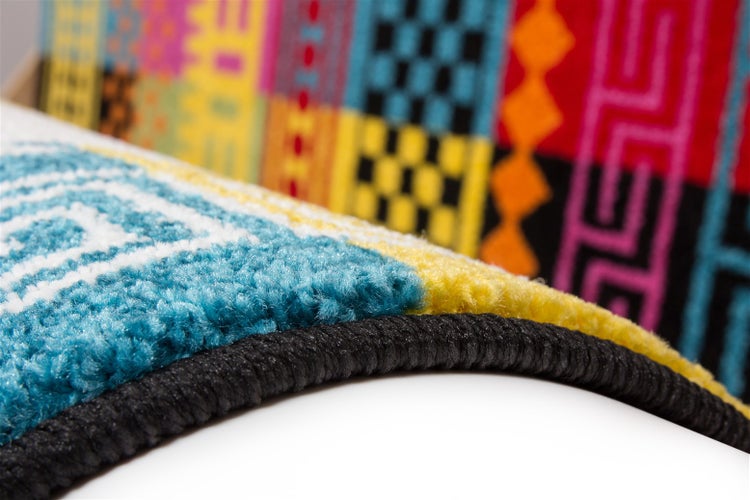 Detailansicht eines Teppichs mit buntem, geometrischem Muster und gekettelter Kante.