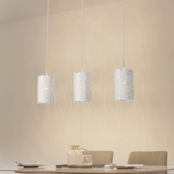 Drei weiße Pendelleuchten mit Muster über einem Esstisch.