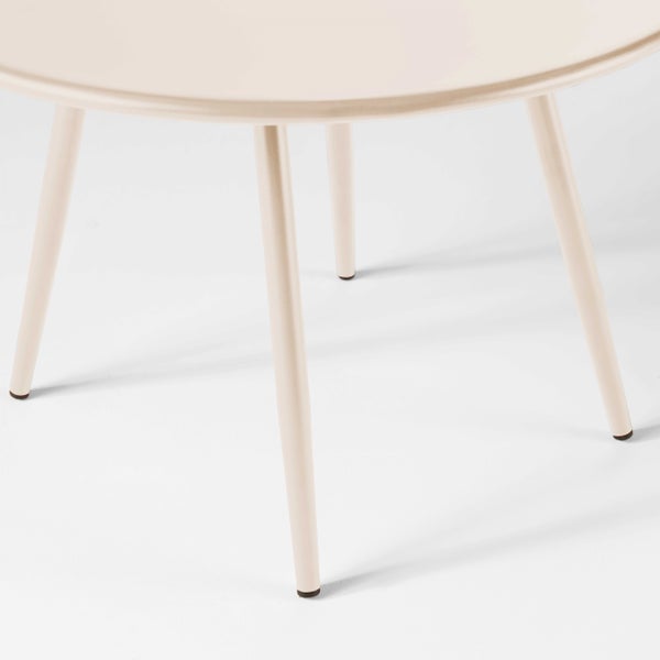 Detailansicht eines runden Metalltischs mit vier schmalen Beinen und einem Teil der Tischplatte.