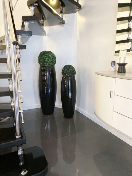 Moderner Flur mit zwei hohen glänzenden schwarzen Pflanzgefäßen mit künstlichen Buchsbaumkugeln, einer Treppe und einem weißen Sideboard.