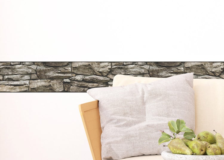 Selbstklebende Bordüre in Steinoptik an einer Wand hinter einem Sofa mit Kissen.