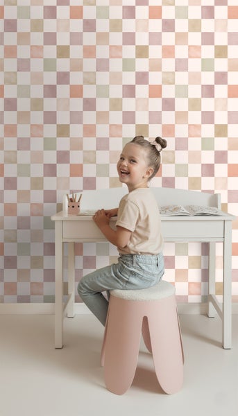 Kind sitzt an Schreibtisch vor Tapete mit Schachbrettmuster