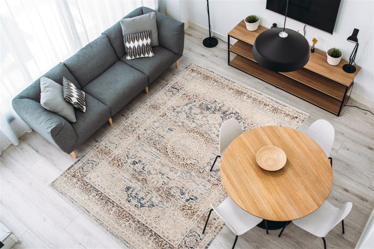Wohnzimmer mit grauem Sofa, rundem Holztisch und orientalisch gemustertem Teppich. Helles, modernes Design mit Holz- und Metallelementen.