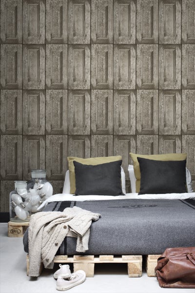 Schlafzimmer mit Holztäfel-Tapete, Bett auf Paletten und dekorativen Glühbirnen in Glasbehältern.