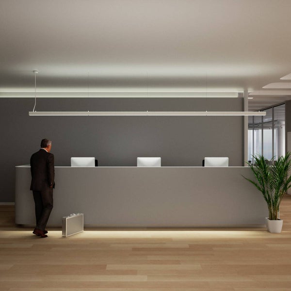 Lange lineare LED-Pendelleuchte über einem Empfangstresen in einem modern gestalteten Büro mit Holzfußboden.