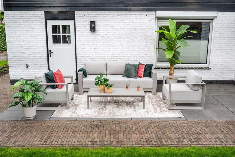 Garten-Lounge-Set aus grauem Aluminium: Dreisitzer-Sofa, zwei Sessel und Couchtisch auf einer Terrasse mit Außen-Teppich und Pflanzen.