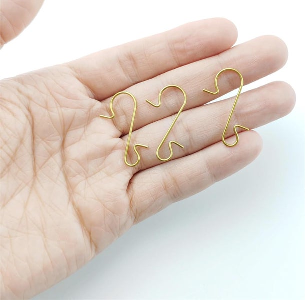 Drei goldfarbene S-Haken auf einer Hand