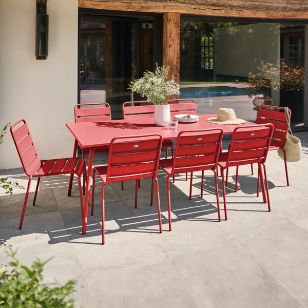 Rote Garten-Essgruppe aus Metall mit rechteckigem Tisch und acht Stühlen auf einer Steinterrasse vor einem modernen Haus mit Pool.