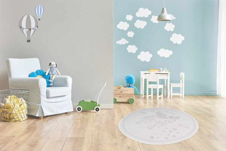 Kinderspielzimmer mit einem runden Teppich mit Einhornmotiv, einem Sessel, einem Kindertisch mit Stühlen und Wandaufklebern mit Wolken und Ballons.