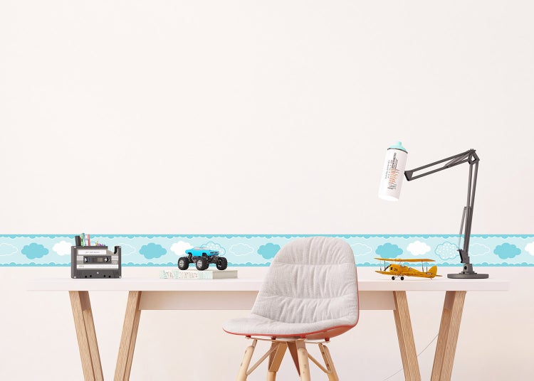 Tapetenbordüre mit Wolkenmotiv an einer Wand über einem Schreibtisch mit Spielzeug und einer Lampe.