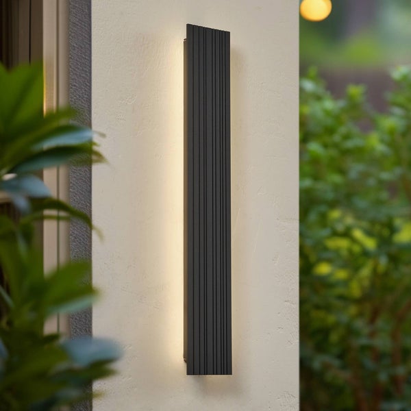 Moderne LED-Außenwandleuchte in Schwarz mit vertikalen Rillen und indirektem warmem Licht, an einer Außenwand montiert.