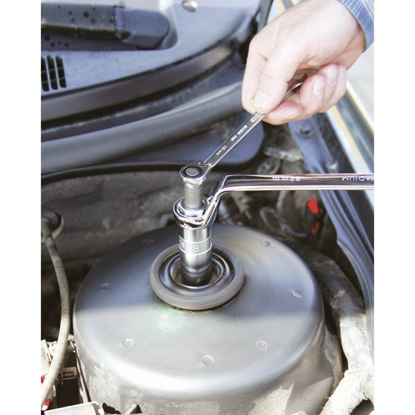 Eine Hand benutzt einen Ratschenschlüssel an einem Stoßdämpferturm im Motorraum eines Autos.