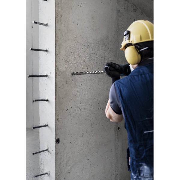 Ein Bauarbeiter bohrt mit einem Bohrer ein Loch in eine Betonwand.