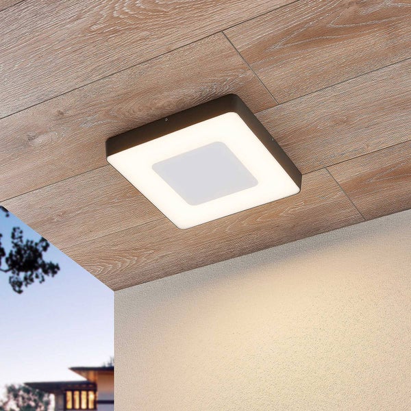 Moderne quadratische LED-Deckenleuchte an einer Holzdecke im Außenbereich, die helles Licht auf eine verputzte Wand wirft.