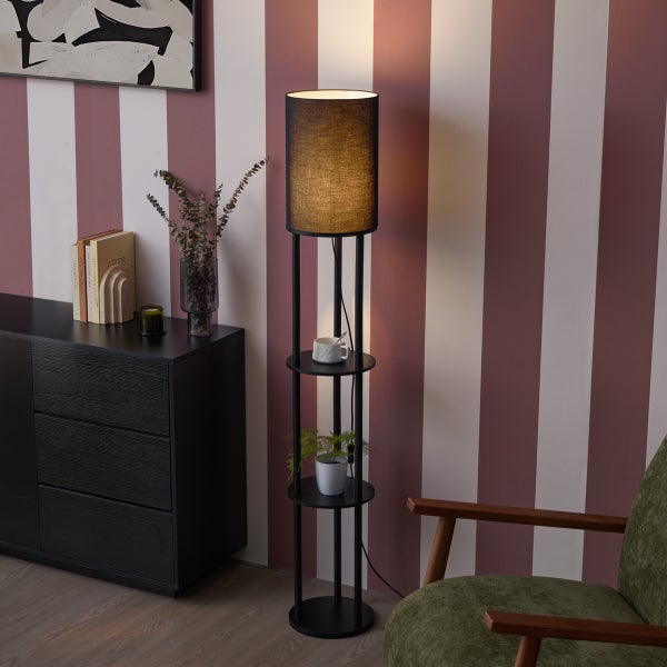 Moderne Stehlampe mit integrierten Ablageflächen, neben einem dunklen Sideboard und einem Sessel in einem Wohnzimmer.