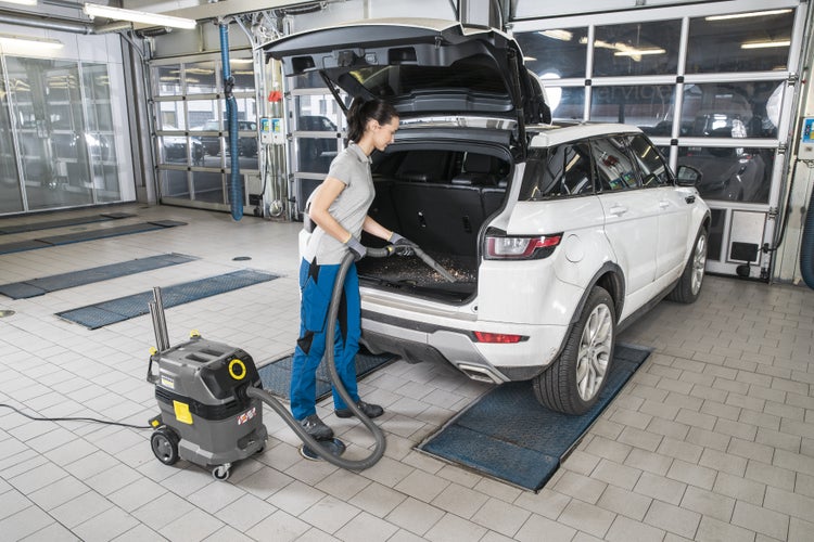 Eine Person reinigt den Kofferraum eines weißen Autos mit einem Kärcher Nass- und Trockensauger in einer hellen Werkstatt.