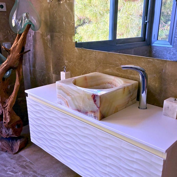 Modernes Badezimmer mit quadratischem Naturstein-Aufsatzwaschbecken aus Onyx auf einem weißen Unterschrank mit Wellenstruktur und Chrom-Armatur.
