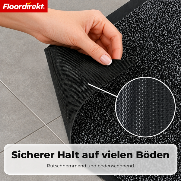 Eine Hand hebt die Ecke einer Floordirekt Fußmatte an, um die rutschhemmende strukturierte Unterseite zu zeigen. Floordirekt Logo.