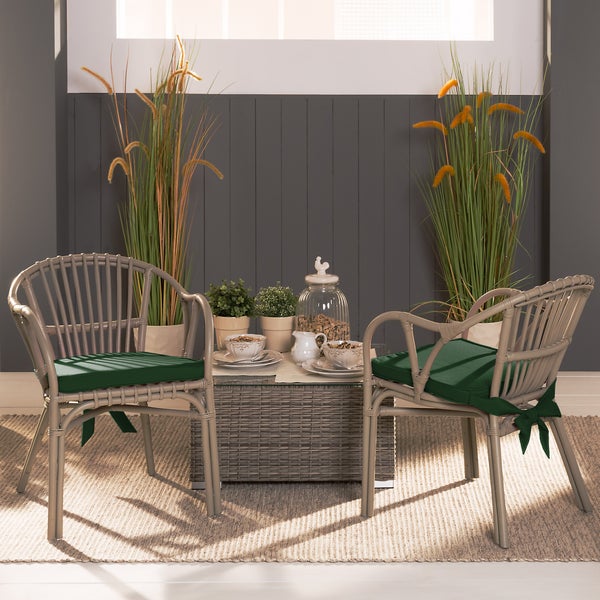 Zwei Gartenstühle in Rattan-Optik mit grünen Sitzkissen und ein passender Wicker-Tisch mit Glasplatte in einer hellen Szene.