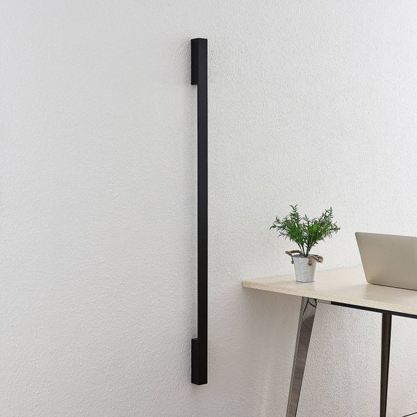 Moderne schwarze LED-Wandleuchte in langer, schmaler Form an einer weißen Wand neben einem Schreibtisch.