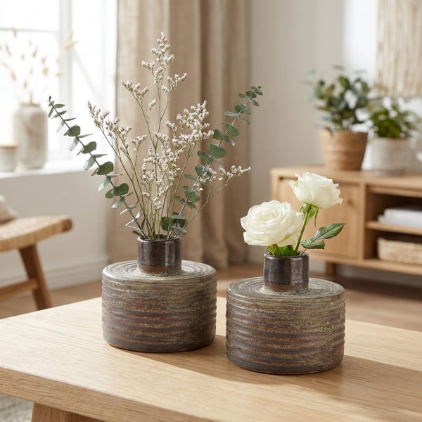 Zwei flache, runde Keramikvasen mit gerillter Struktur stehen auf einem Holztisch, dekoriert mit Trockenblumen und weißen Rosen.