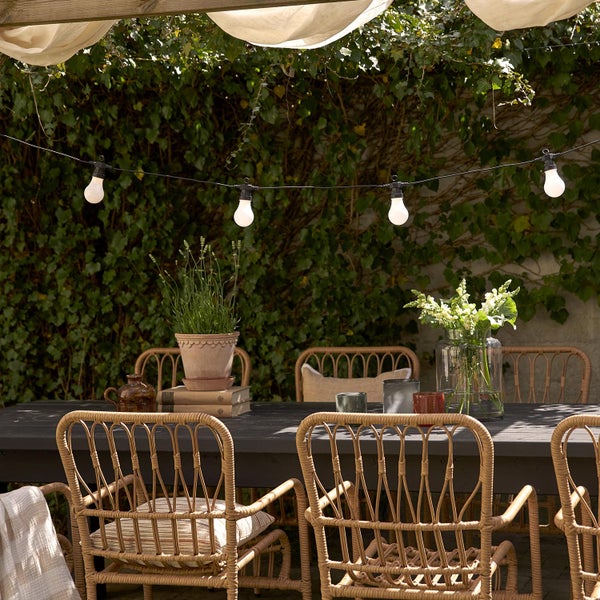 Gartenszene mit Esstisch, Rattan-Stühlen und Lichterkette
