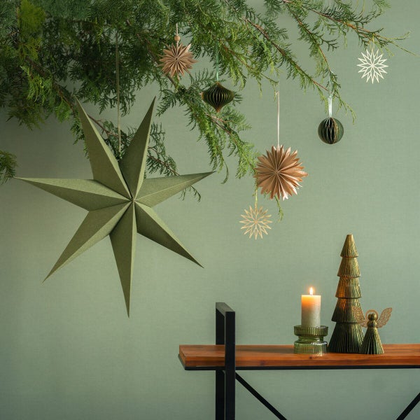 Weihnachtliche Tischdekoration mit Papiersternen, Tannenbaum-Figur, Kerze und Engel-Figur unter einem Tannenzweig arrangiert.